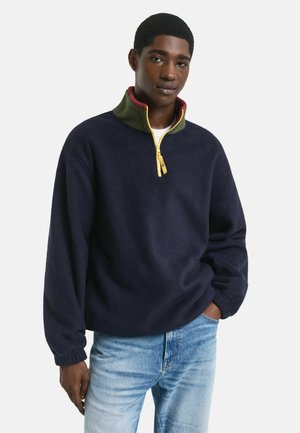 Navy fleece pullover with a half-zip collar; green and red accents; relaxed fit with ribbed cuffs and a textured finish.