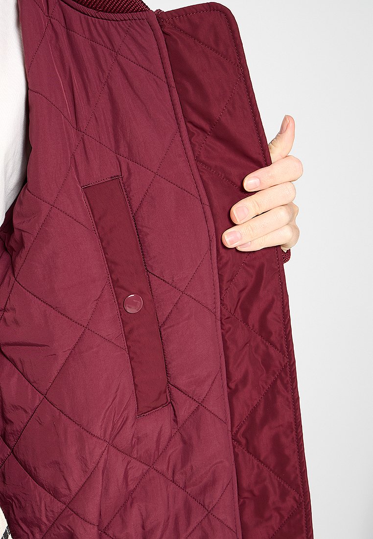 Veste matelassée bordeaux avec une surface texturée, une poche boutonnée à l'intérieur et un col côtelé.