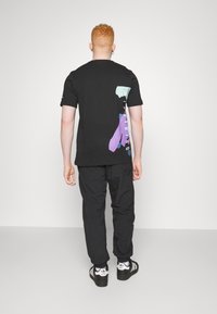 Černé tričko s krátkým rukávem a vícebarevným grafickým vzorem na zádech. Doplněno volnými černými kalhotami a černými teniskami.