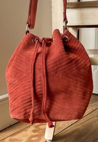 Väskan i rostfärgad mocka har texturerade horisontella linjer, dragskoöppning och metalliska hårdvaruaccents.