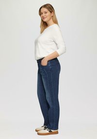 Witte lange mouwen top, blauwe spijkerbroek met een rechte snit, met voorzakken. Schoenen zijn beige met zwarte accenten en rubberen zolen.