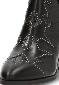 Botas de vaquero de cuero negro con tachuelas plateadas que delinean patrones decorativos de hojas texturizadas y estrellas en la punta y el costado.