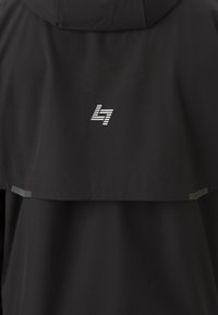 Μαύρο μπουφάν με κουκούλα, λεία υφή και λευκό διακοσμητικό λογότυπο στο επάνω μέρος της πλάτης. Περιλαμβάνει διακριτικά ανακλαστικά στοιχεία.