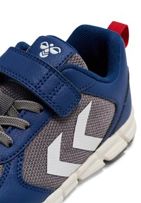 Niebieski but sportowy z materiałów skórzanych i siateczkowych, z szarymi akcentami, paskiem na rzep oraz białym zygzakowatym wzorem po boku.