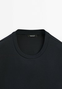 Černé tričko s krátkým rukávem a kulatým výstřihem, s viditelnou nálepkou Massimo Dutti na zadním límci, prezentované ležící na bílém pozadí.