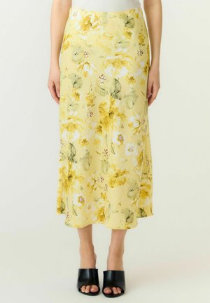 Gul midi-skjørt med grønt og hvitt blomsterprint, brukt med svarte åpne hælsko med åpen tå.