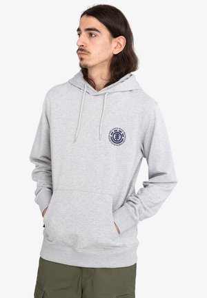 Sudadera gris claro con un bolsillo frontal, capucha con cordón y un logo circular en azul marino en el pecho. Presenta puños y dobladillo acanalados.