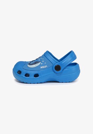 Zoccoli in gomma blu con design di una balena, perforazioni per la ventilazione, un cinturino posteriore e suola testurizzata per la presa. Etichetta del marchio sul lato.