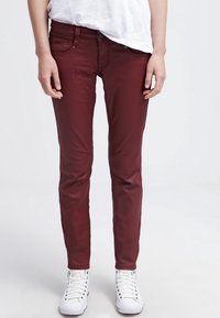 Burgundy slim-fit jeans gjorda av en bomullsblandning, med fem fickor och dragkedja, parat med vita högskurna sneakers.