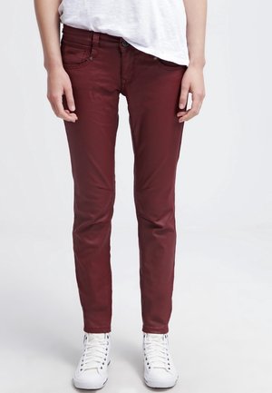 Burgundowe dżinsy slim-fit wykonane z tkaniny bawełnianej, posiadające pięć kieszeni oraz zamek błyskawiczny, w zestawieniu z białymi trampkami za kostkę.