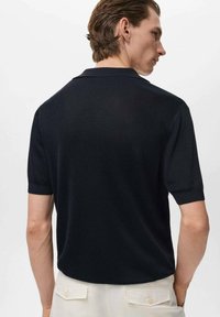 Polo de manga corta en un oscuro color navy, confeccionado en un tejido de punto texturizado con un cuello clásico, visto desde la parte posterior. Diseño liso y minimalista.