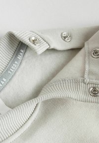 Ljusgrå tröja med ribbat halsband och knäppningar. Mjuk, texturerad textil med en fluffig insida. Märket säger "TEDDY BEAR."