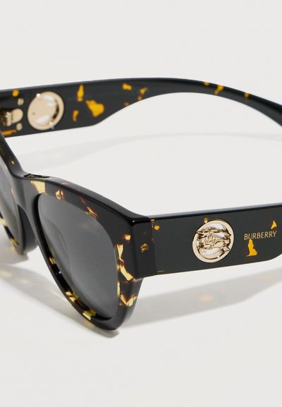 Ορθογώνια γυαλιά ηλίου σε σκούρο καφέ σχέδιο χελώνας με χοντρά πλαϊνά, χρυσό έμβλημα και το κείμενο "BURBERRY" στο πλάι.