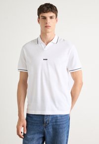 Biela polo košeľa s krátkym rukávom a textúrovaným pleteným dizajnom, s golierom s modrým lemovaním a logom "BOSS" na hrudi.
