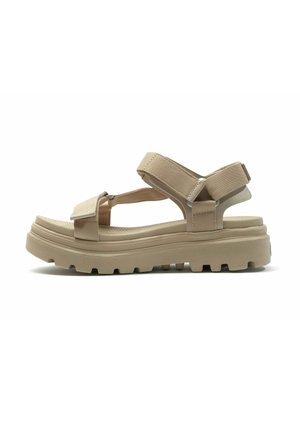 Beige Sandalen mit verstellbaren Stoffriemen, einer stabilen Gummi-Sohle und einem strukturierten Fußbett. Sie bieten ein unterstützendes Design mit robustem Halt.