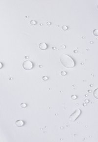 Duidelijke waterdruppels van verschillende groottes op een gewatteerd witte ondergrond, die een patroon creëren tegen de lichte achtergrond.