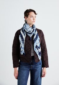 Istezani smeđi kaput, sivi gornji dio i plavi/bijeli šal s resicama. Šal sadrži cvjetne i geometrijske uzorke. Traperice.