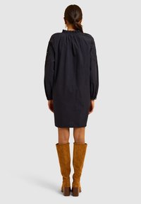 Abito in cotone navy con maniche a palloncino e scollatura arricciata, abbinato a stivali al ginocchio in suede marrone con tacchi spessi.