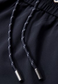 Un tissu noir au toucher lisse présente des cordons de serrage dans un motif tressé, se terminant par des embouts en métal argenté.