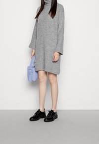 Abito grigio a collo alto in maglia con maniche lunghe, abbinato a una piccola borsa color lavanda e scarpe nere stringate con suole spesse.