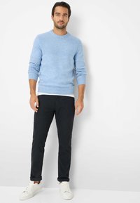 Hellblauer Strickpullover mit gerippter Textur, kombiniert mit dunklen Hosen und weißen Sneakers. Der Pullover hat einen schlichten Rundhalsausschnitt.
