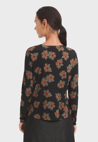 Woman with dark hair in a ponytail wearing a black long-sleeve top with brown, gray, and red floral patterns, facing away from the camera.