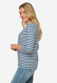 Randig topp i blått och vitt, med rund halsringning och trekvartslånga ärmar, i kombination med ljusblå jeans. Mjuk tygkänsla.