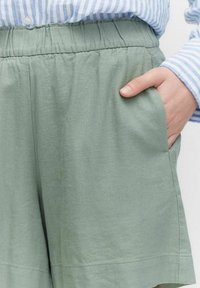 Ljusgröna shorts gjorda av mjukt material med elastisk midja och sidofickor. Tyget har en slät textur och en avslappnad design.