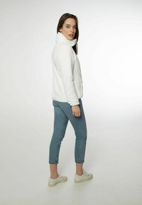 Giacca in fleece bianca con colletto alto, tasche frontali e una texture morbida. Abbinata a jeans fitted azzurri e sneakers bianche.