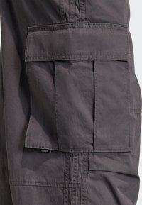 Sivé cargo šortky s veľkým bočným vreckom, vyrobené z odolnej látky s viditeľnými detailmi švov a malou značkovou etikou.