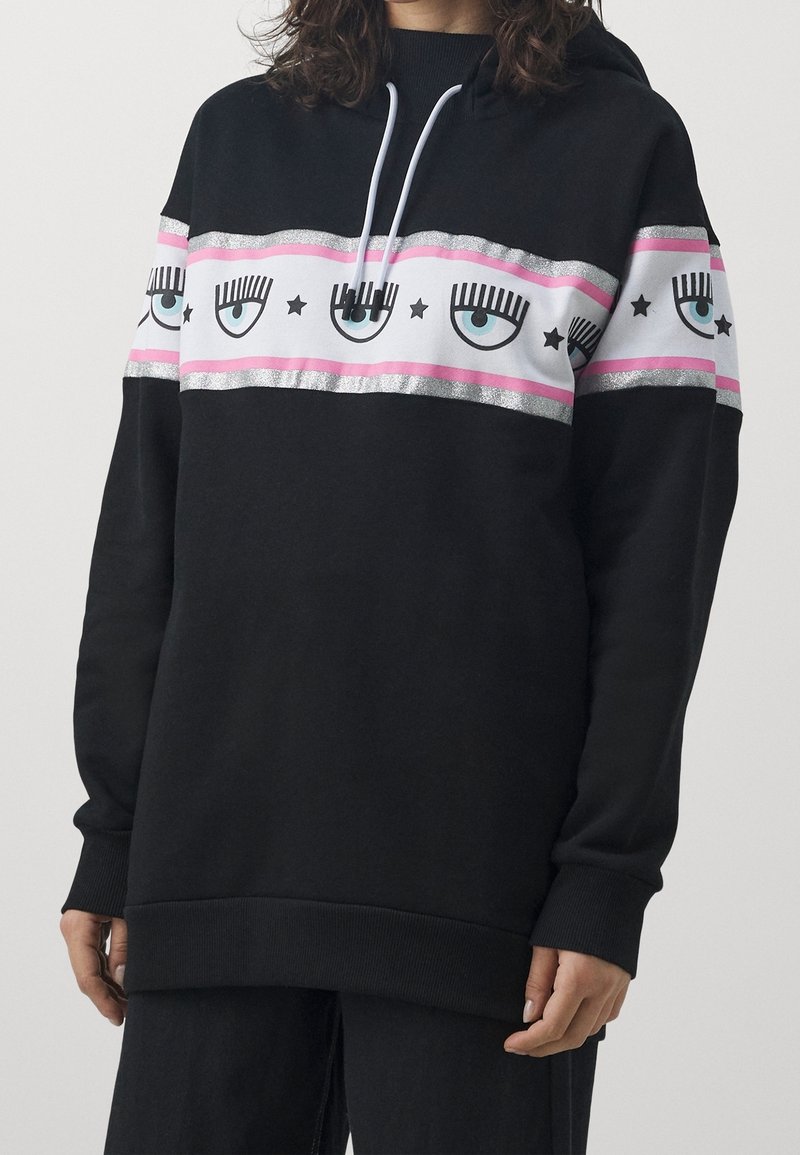 Sweat à capuche noir avec un motif avant comprenant des rayures roses et argentées, des graphismes d'yeux et des étoiles. Confectionné en tissu doux avec une coupe décontractée.