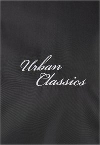 Tela negra con el texto bordado "Urban Classics" en una fuente cursiva blanca, de textura suave y sin patrones adicionales ni herrajes.