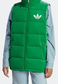 Grön uppblåsbar väst med hög krage och frontdragkedja. Har horisontella quiltade sektioner och vit Adidas trefoil-logotyp på bröstet.