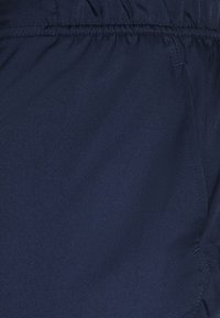 Tela azul oscura con una textura suave, que presenta costuras cosidas y una cinturilla fruncida para un ajuste ajustable. Sin patrones ni acentos adicionales.