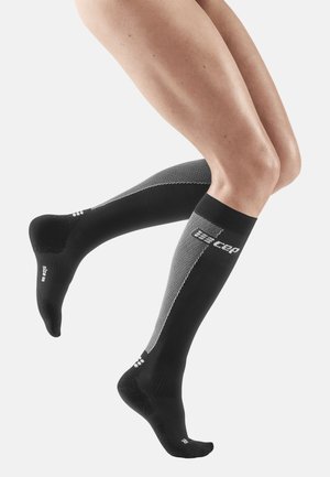 Schwarze und graue Kompressionssocken mit einem strukturierten Muster, featuring weißen Branding und einem enganliegenden Sitz, der bis knapp unter das Knie reicht.