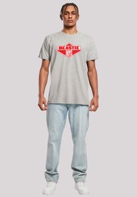 Gray cotton t-shirt featuring a red "BEASTIE BOYS" graphic on the front; paired with light blue jeans and white sneakers.
