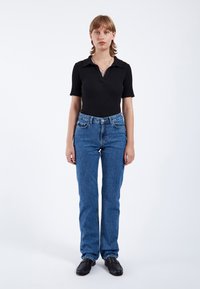 Camiseta polo negra con acanalado y mangas cortas, combinada con jeans de mezclilla azul de tiro alto y zapatos de cuero negros. Diseño simple y ajustado.