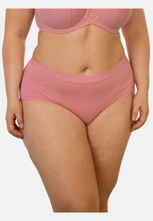 Frau trägt ein passendes rosa BH- und hoch tailliertes Unterwäscheset, gezeigt von der Mitte des Oberschenkels bis zur Mitte des Oberkörpers vor einem einfarbigen Hintergrund.