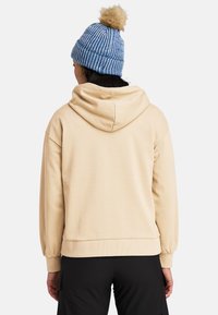 Beige hoodie med lös passform, i bomullsmaterial, och en stor huva. Bärs med en blå randig stickad mössa med en tofs.