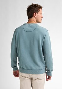 Felpa azzurra chiara con girocollo, rifinita con polsini e fondo a coste, caratterizzata da una texture liscia e un dettaglio di yoke rotondo sul retro.
