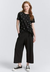 Czarna koszulka z małymi białymi wzorami serc, w połączeniu z luźnymi czarnymi spodniami typu wide-leg i czarno-białymi trampkami.