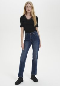 Top nero a coste con maniche a scalloped e scollatura in pizzo, abbinato a jeans blu a vita alta e stivali neri alla caviglia. Design semplice e classico.
