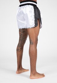 Witte en zwarte sportshorts met een gestructureerd mesh-zijpaneel, elastische tailleband en zijsplitdetails, voorzien van "GORILLA WEAR" branding.