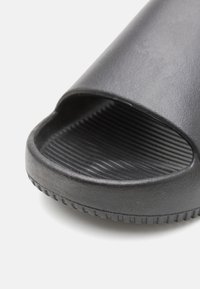 Svart slide sandaler med teksturert finish, åpen tå og buedekanter. Sålen har rillete detaljer for grep og stabilitet.