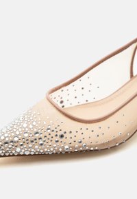 Μπεζ επίπεδη μυτερή γόβα με διάφανα πλαϊνά και ασημένια διακοσμητικά με στρας στο μπροστινό και στα πλαϊνά μέρη.