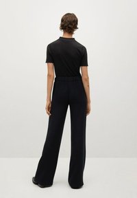 Polo noir à manches courtes avec col festonné, associé à un pantalon noir à jambes larges. Tissu lisse et coupe décontractée. Pas de motifs ni d'accents visibles.