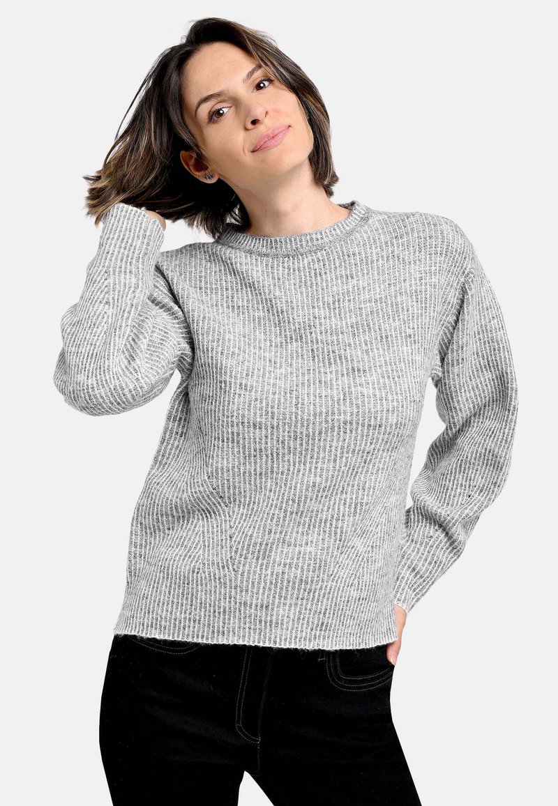 Hellgrauer gestrickter Pullover mit langen Ärmeln, rundem Ausschnitt und strukturiertem Rippenmuster. Kombiniert mit schwarzen Hosen.