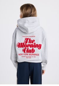 Gray sweatshirt with hood, featuring red embroidered text: "YOUR DAILY FAVORITES The Morning Club NEW YORK MORNINGS." Simple design.