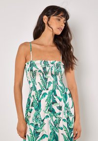 Blomster maxi kjole med grønne bladmønstre på en hvid baggrund. Har en elastisk bodice og tynde stropper. Let og svævende design.