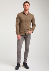 Camicia a maniche lunghe con motivo marrone e bottoni, pantaloni grigi slim-fit e scarpe da ginnastica blu navy. Design semplice con dettagli in bottone.